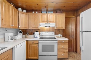 A kitchen with wooden cabinets, a stove, a refrigerator, and a coffee maker. - Oceanfront Beach House in Ocean Drive. LOTS of Charm and amazing views! (North Myrtle Beach)