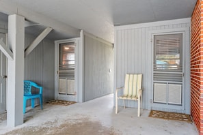 A covered porch with a blue plastic chair, a striped chair, and a concrete floor. - 5BR 4BA OF Beach House. LOTS of Charm (North Myrtle Beach)