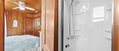 Una habitación de madera con una cama, ventilador de techo y zona de ducha con puerta de cristal.