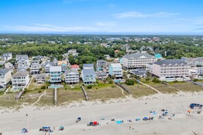 A coastal residential area with beachfront properties, including multi-story buildings with balconies and a sandy beach with umbrellas and beach chairs. - Oceanfront Beach House in Ocean Drive. LOTS of Charm and amazing views! (North Myrtle Beach)