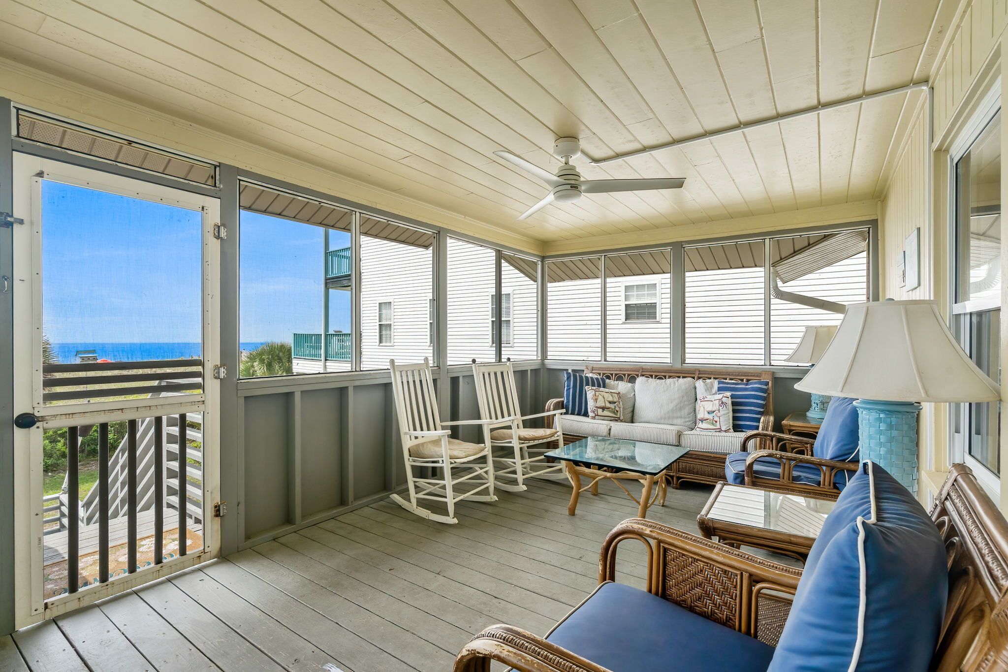 A covered porch with a ceiling fan, wicker furniture, and a view of the ocean.