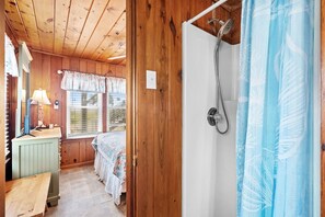 Une pièce aux murs lambrissés, comprenant un lit, un bureau, une lampe et une douche avec un rideau de douche bleu.