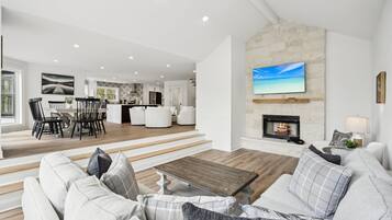 Amplia sala de estar con chimenea, comedor y televisor grande montado en la pared.
