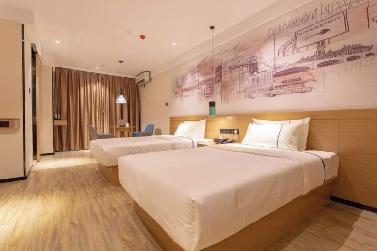 Habitación de hotel con dos camas, cabecero de madera, un mural en la pared, un escritorio y una silla.