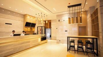 Un hall d’hôtel moderne comprenant un comptoir d’accueil, un bar et un espace détente avec des sièges.