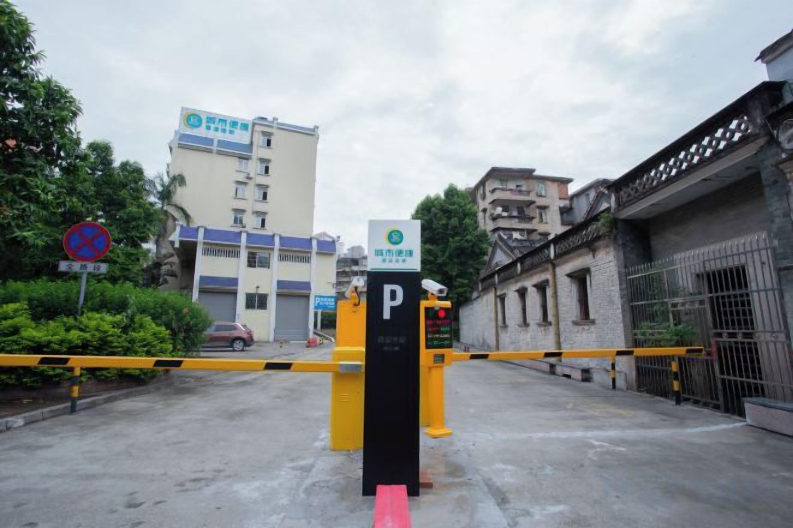 A gated parking area with a yellow barrier, a 'P' sign, and a building with a blue and white facade in the background.