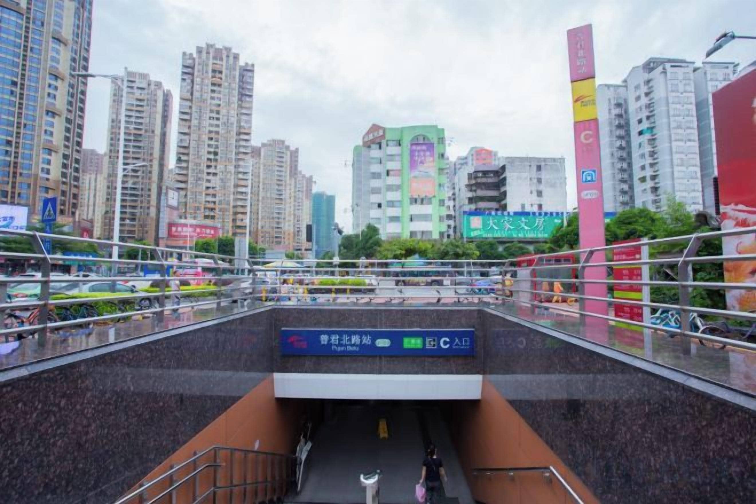 A pedestrian bridge with a ramp leading to a building entrance, surrounded by high-rise buildings and a clear sky.