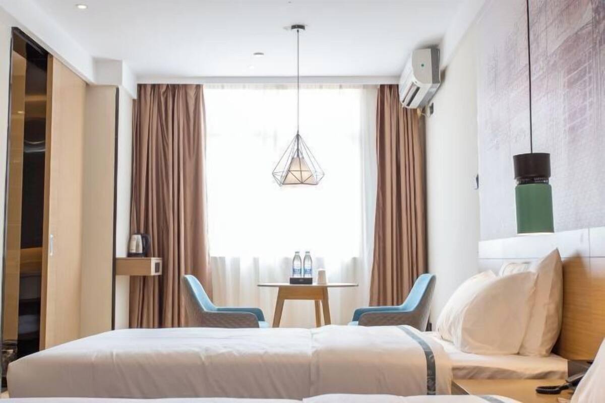 Una habitación de hotel con una cama, dos sillas, una mesa con botellas y una lámpara colgante.