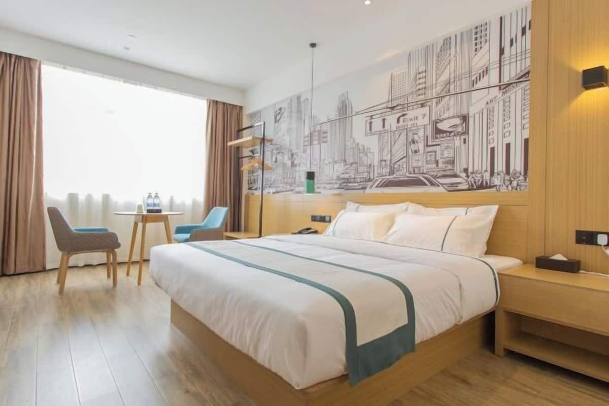 Habitación de hotel con una cama grande, un escritorio, dos sillas, un mural con vista a la ciudad y vistas por la ventana.