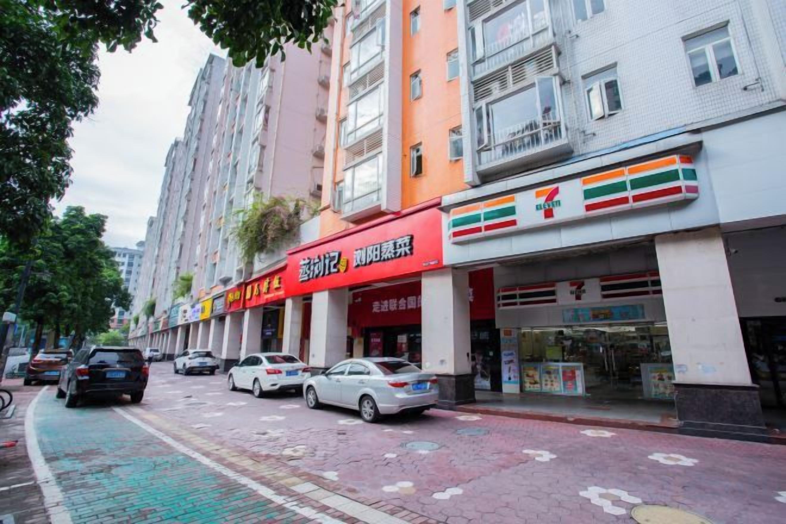 A street with parked cars and a 7-Eleven store.