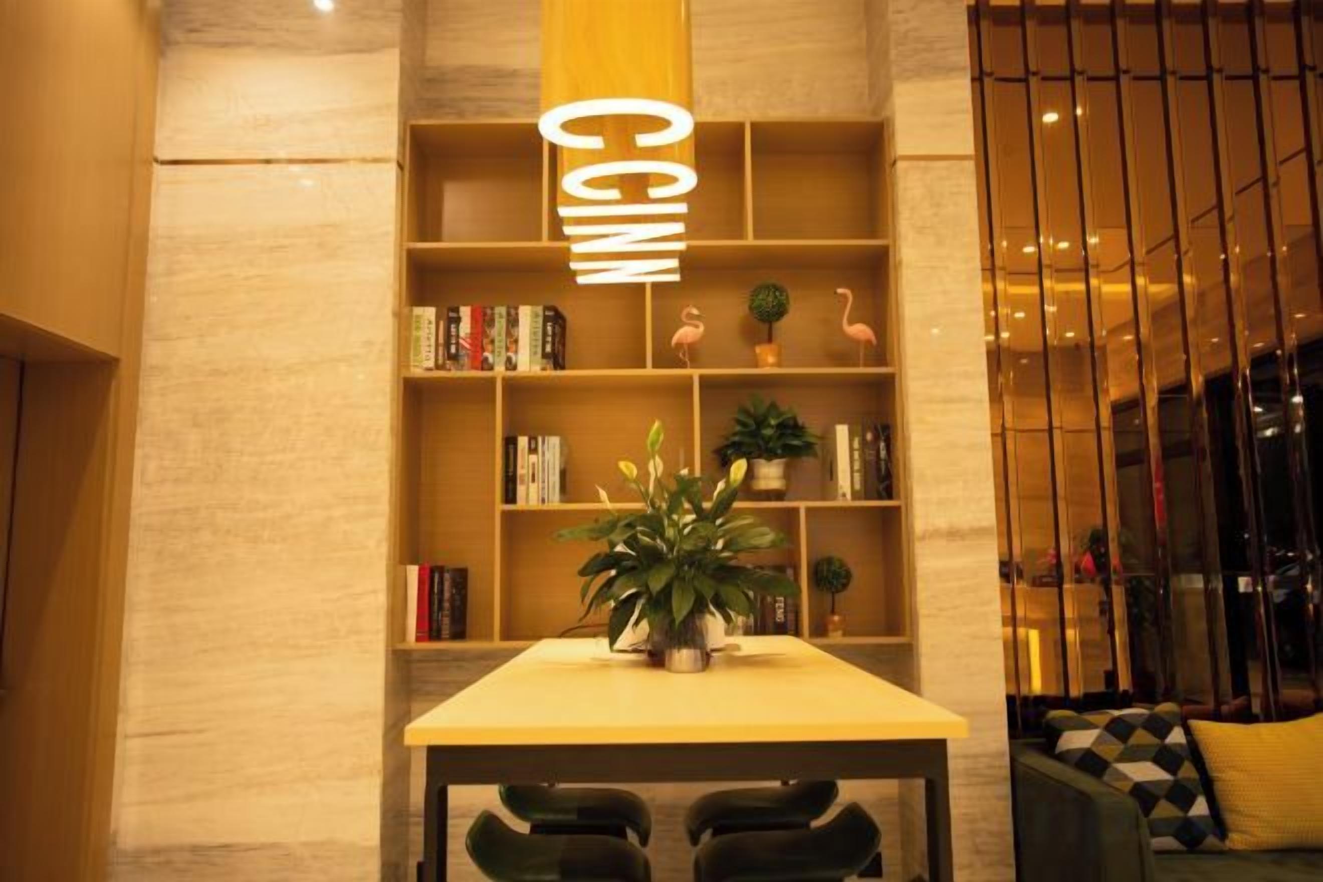 Uma área de recepção com balcão de madeira, planta em vaso e estante com livros e objetos decorativos.