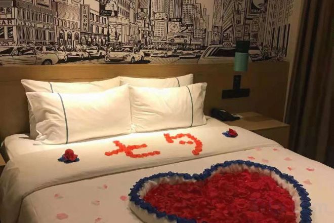 Une chambre d’hôtel avec un lit agrémenté d’une décoration en forme de cœur et un mur orné d’une fresque représentant un paysage urbain.