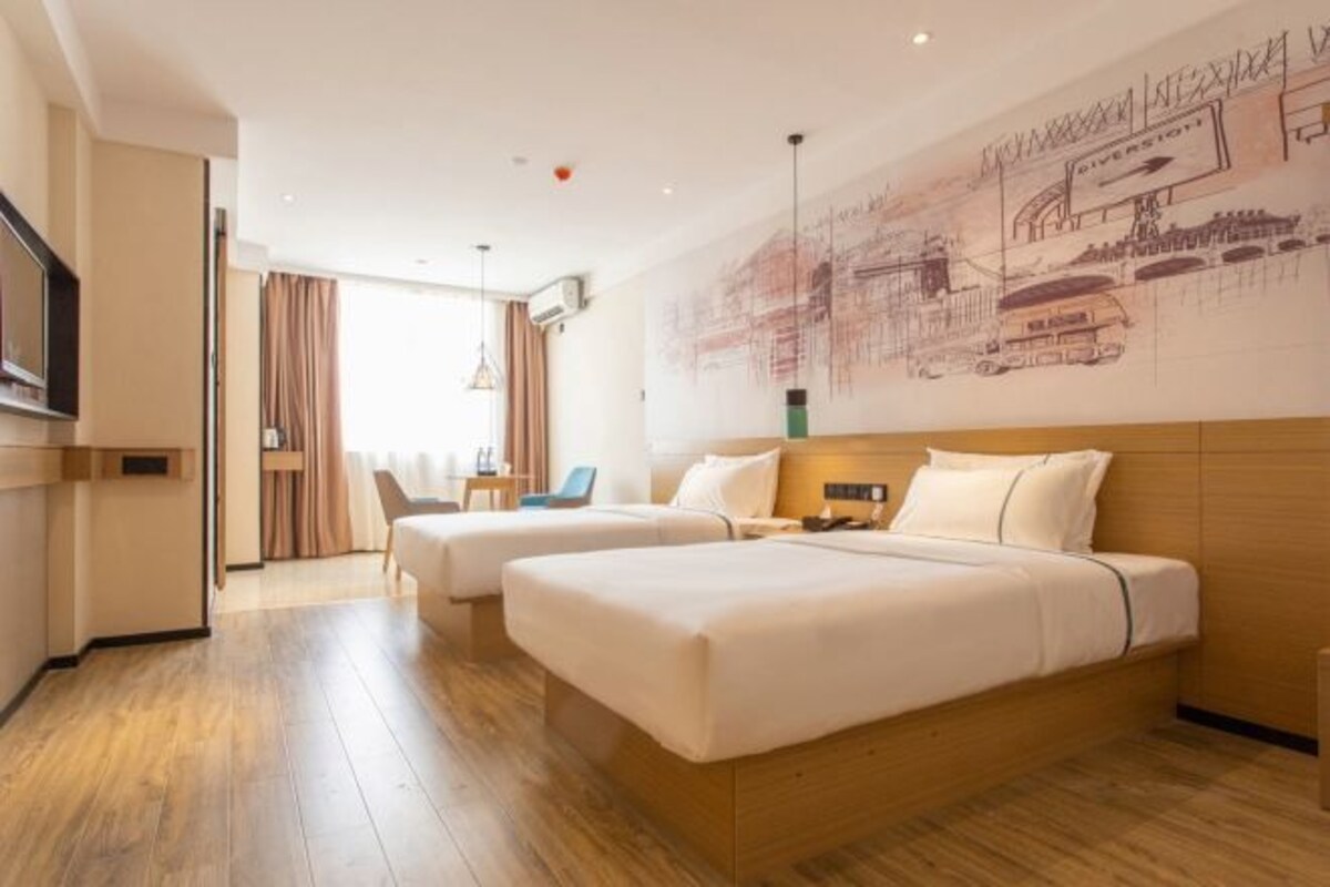 A hotel room with two beds, a wooden floor, a large wall mural, a TV, and a desk with a chair.