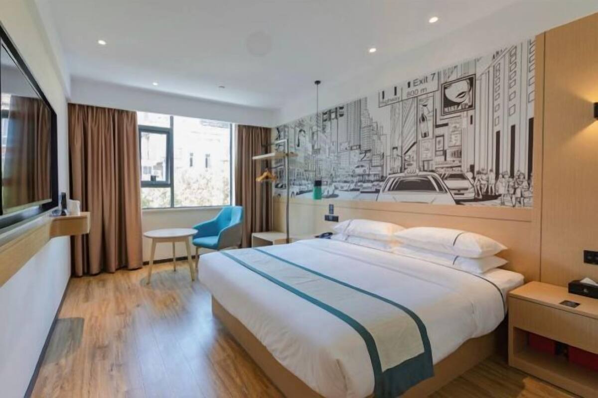 Habitación de hotel con cama, escritorio, silla, ventana y un mural en la pared.
