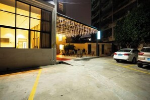 Un edificio con una entrada amplia y abierta, un estacionamiento con coches y una señal de calle visible.