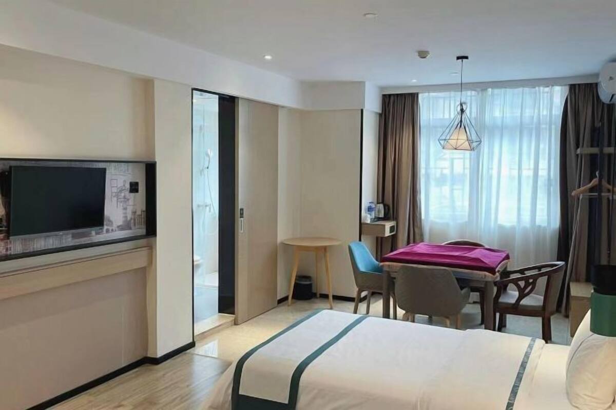 Habitación de hotel con cama, escritorio, silla, televisor y ventana con cortinas.