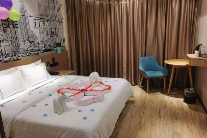 Une chambre d’hôtel avec un lit, une chaise bleue, une petite table et un rideau.