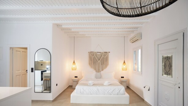 A modern bedroom with a large bed, bedside lamps, a hanging macrame wall piece, and a large mirror. - Loom Suite Ornos Mykonos (Mykonos)