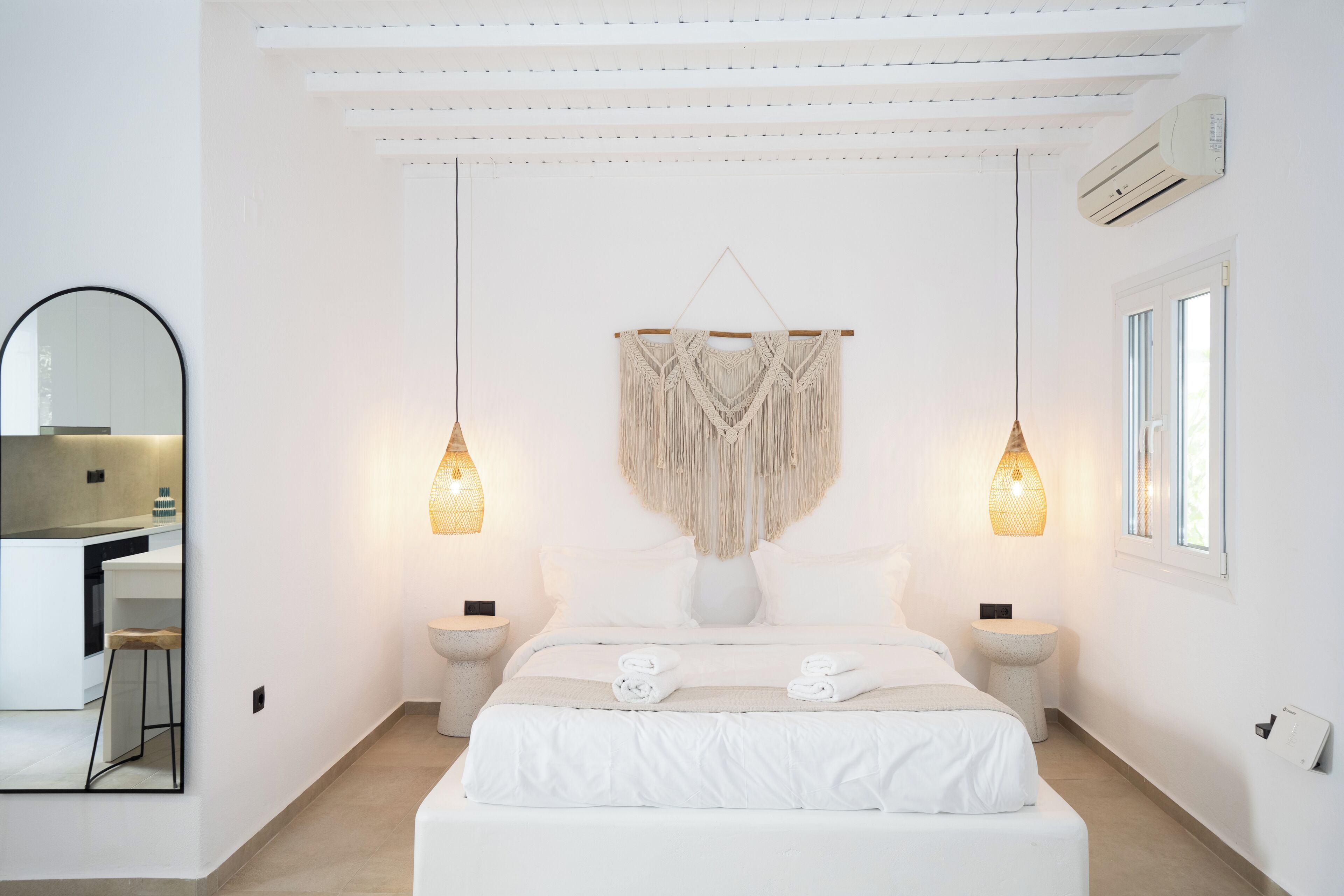 Un dormitorio moderno con una cama grande, dos mesitas de noche, un adorno colgante de macramé y un espejo amplio.