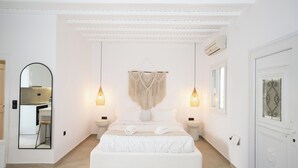 A spacious bedroom with a large bed, two bedside tables, a hanging macrame wall decoration, and a large mirror. - Loom Suite Ornos Mykonos (Mykonos)