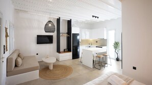 A modern, open-plan living space with a sofa, dining table, kitchen, and a bed. - Loom Suite Ornos Mykonos (Mykonos)