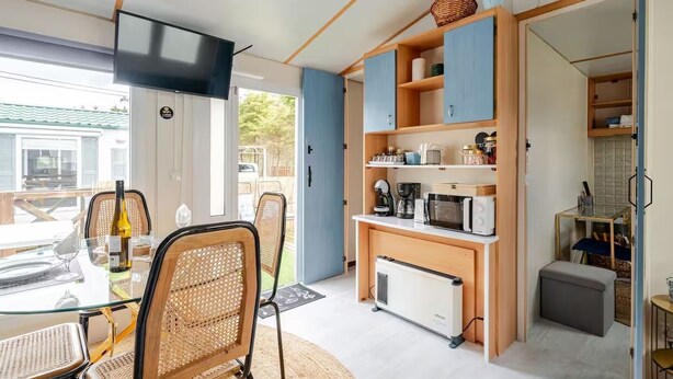 A compact living space with a dining area, kitchenette, and a TV mounted on the wall. - Casa azul (Pataias)