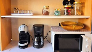 A kitchen with a microwave, coffee maker, and a coffee pot. There are jars on the shelf and a wooden bowl on the counter. - Casa azul (Pataias)