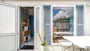 A compact, modern home with a small kitchen, a dining area with a table and chairs, and a large window with shutters. - Casa azul (Pataias)