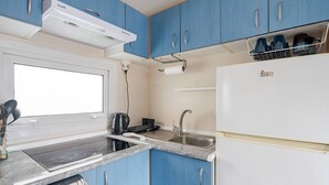 A compact kitchen with blue cabinets, a white refrigerator, a built-in stove, and a window. - Casa azul (Pataias)