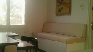 A room with a white sofa, a small table, and a chair. There is a window with a view of trees outside. - Waterfront duplex with sea view EXTRAORDINARY (Monastir)