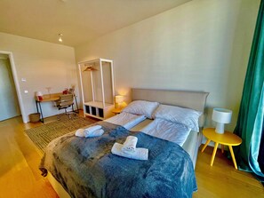 A hotel room with a bed, a desk, a chair, a lamp, and a green curtain.