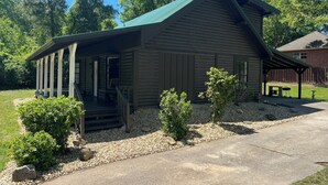 Un rustico chalet con un portico, circondato da ghiaia e piccoli arbusti.