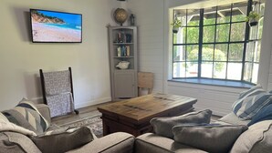 Un soggiorno con divano, tavolino, libreria e televisione che mostra una spiaggia.
