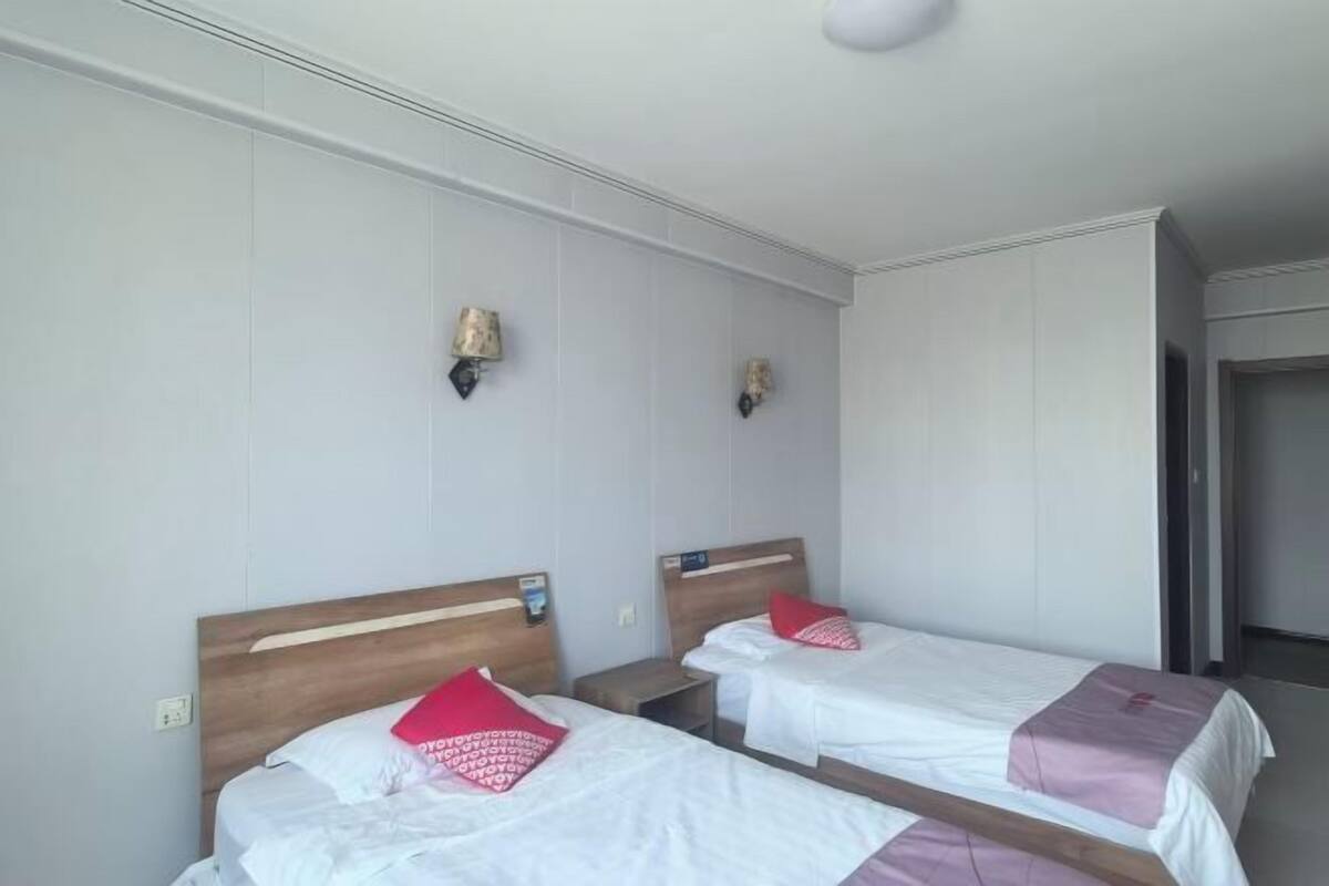 Ett hotellrum med två separata sängar, var och en med en sänggavel i trä och vitt sänglinne. Det finns två väggmonterade lampor och en spegel ovanför sängarna.