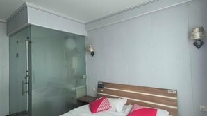 Una habitación de hotel con cama, cabina de ducha de vidrio y mesita de noche.
