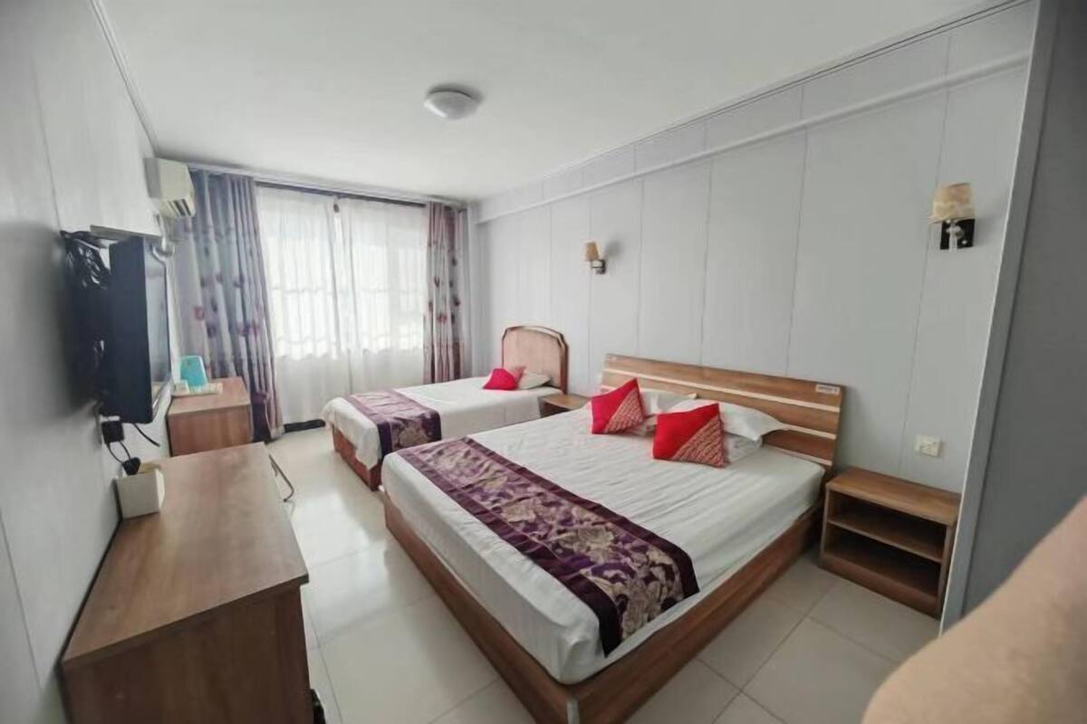 Ett hotellrum med två sängar, ett skrivbord i trä, en TV och ett fönster med gardiner.