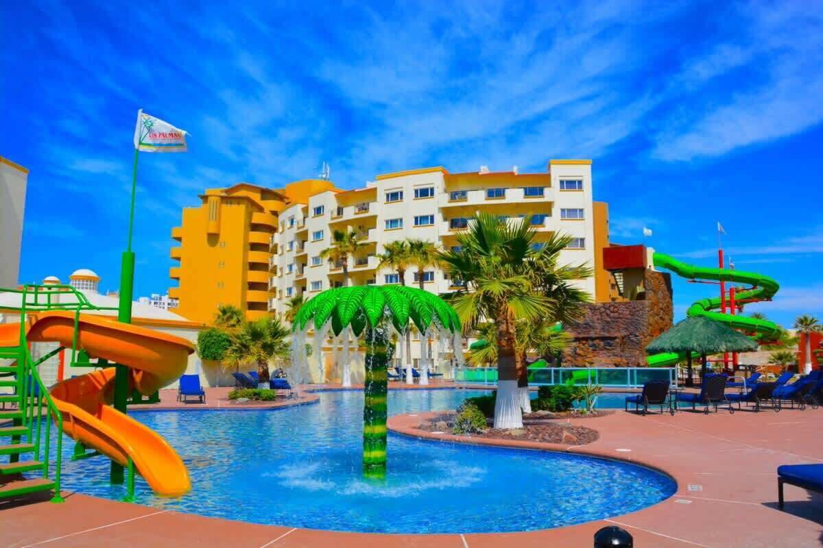 A hotel pool area with a water slide, palm trees, and a flag.