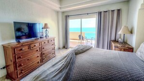 Ein Hotelzimmer mit einem Bett, einem Fernseher auf einer Holzkommode, einer Lampe und Meerblick durch eine Schiebetür.