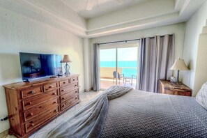 A hotel room with a bed, a TV on a wooden dresser, a lamp, and a view of the ocean through a sliding door.