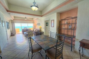 A dining area with a large table, chairs, a ceiling fan, and a view of the ocean.