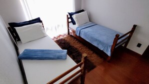 Une petite pièce bien éclairée, avec deux lits simples, une chaise en bois et un tapis en fourrure sur le sol.