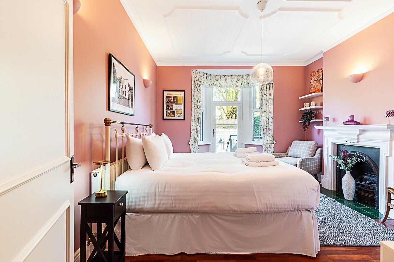 Une chambre à coucher avec un grand lit, une cheminée et une fenêtre ornée de rideaux à motifs floraux.