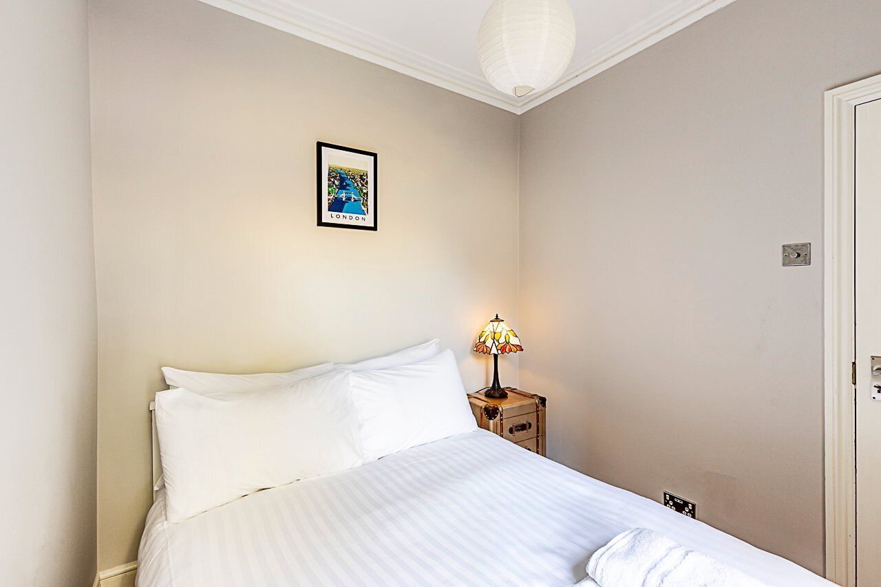 A neatly made bed with white linens, a framed picture on the wall, and a bedside lamp.