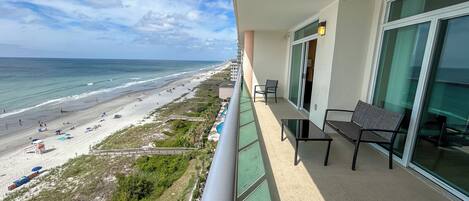 Un balcon avec vue sur la plage, une porte vitrée et une chaise.