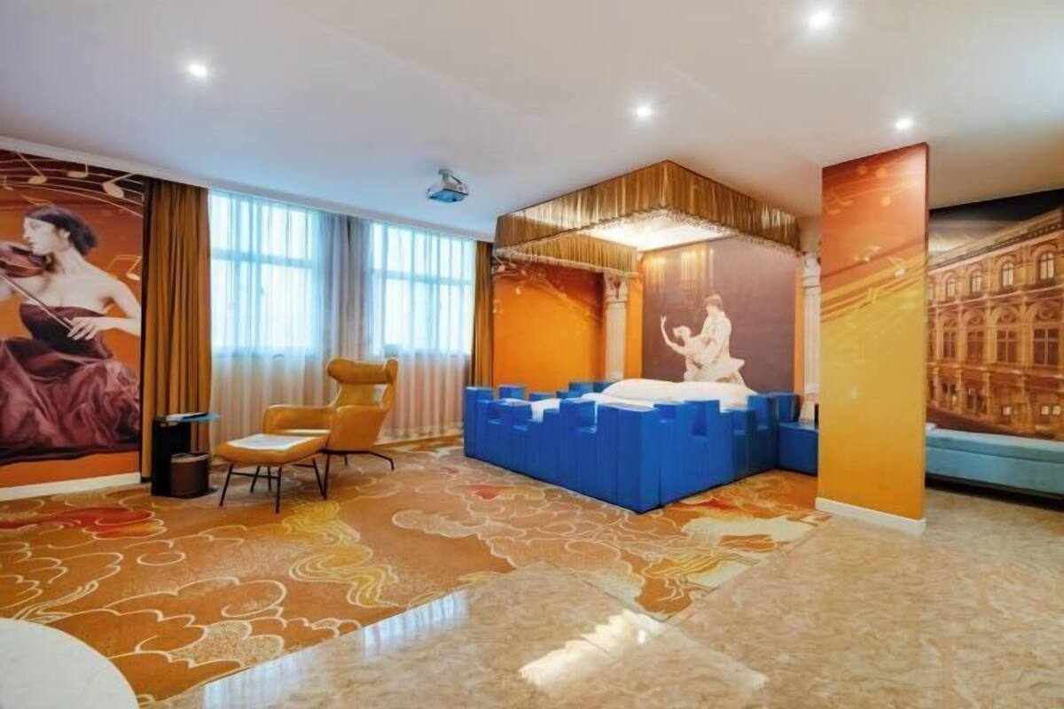 A hotel room with a large bed, a chair, a small table, a decorative wall mural, and a large window.