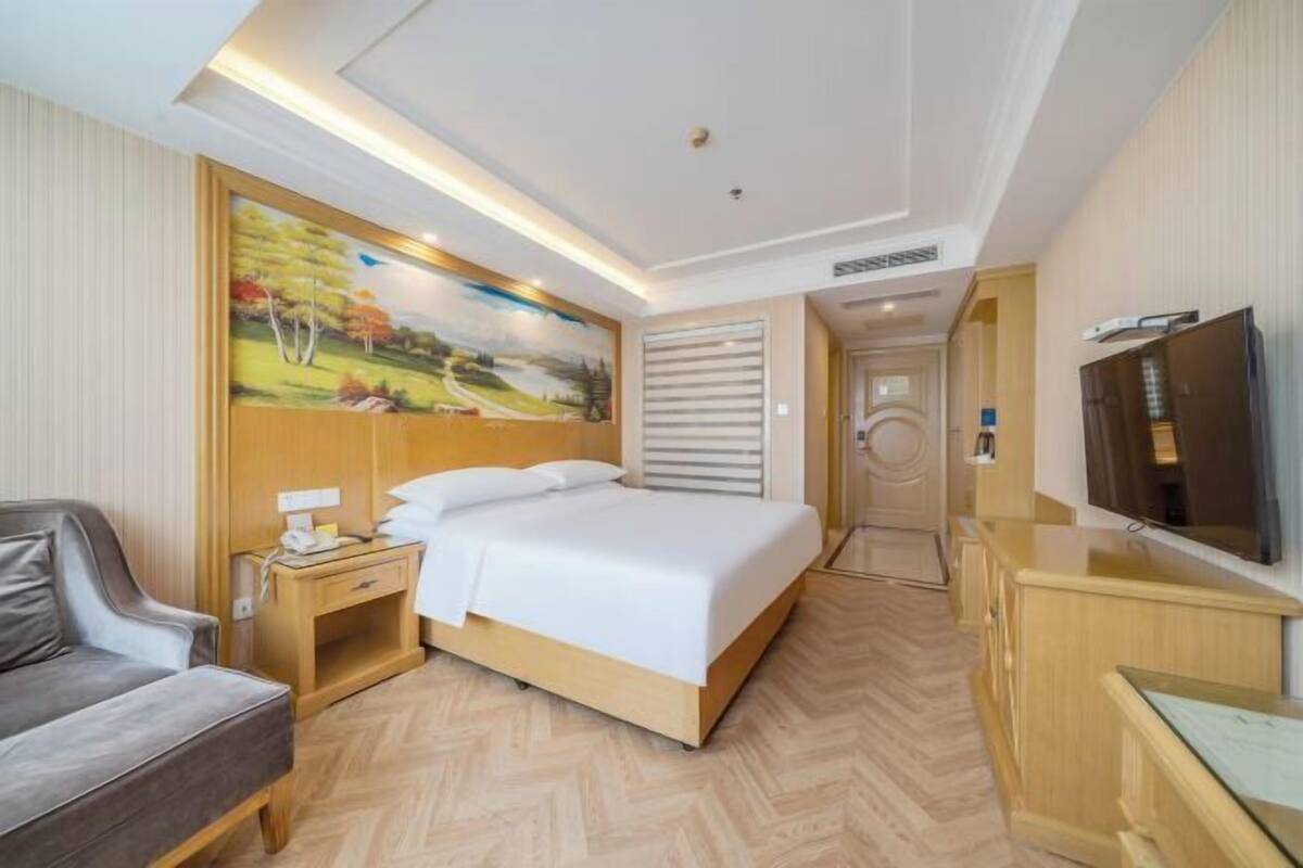 A hotel room with a bed, a desk, a chair, a TV, and a painting on the wall.