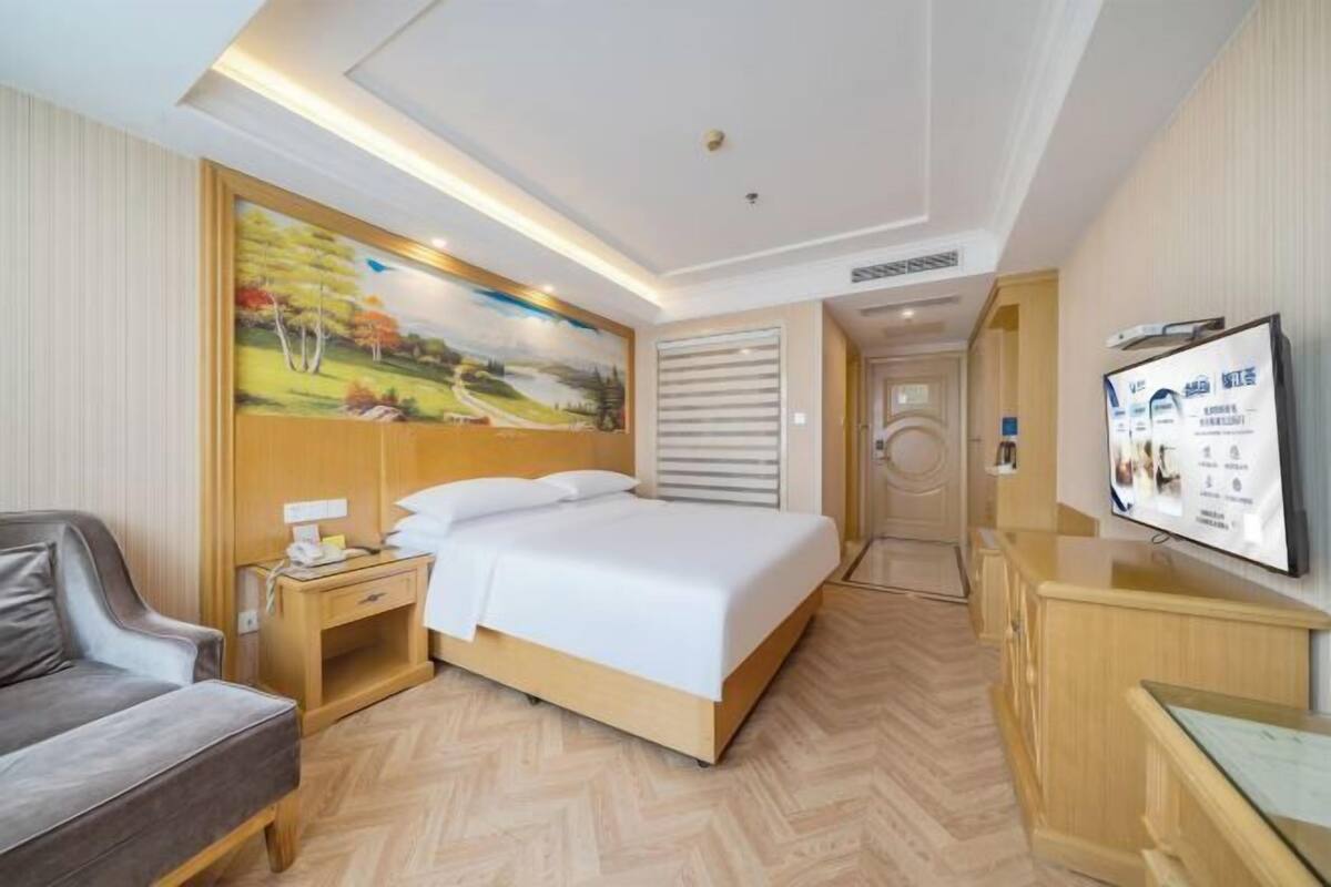 A hotel room with a bed, a desk, a chair, a TV, and a painting on the wall.