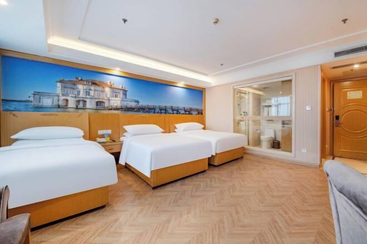 A hotel room with two beds, a large window, and a mural of a coastal scene.