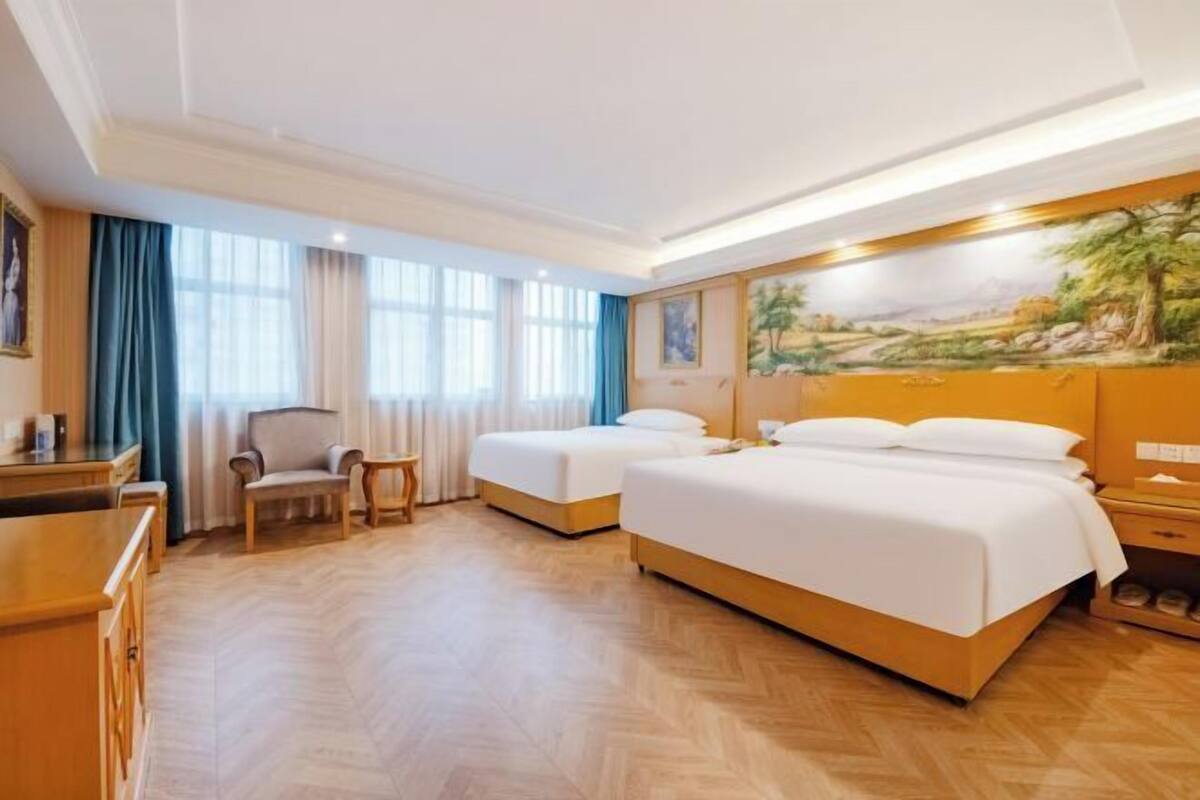 A hotel room with two beds, a desk, a chair, and a painting on the wall.