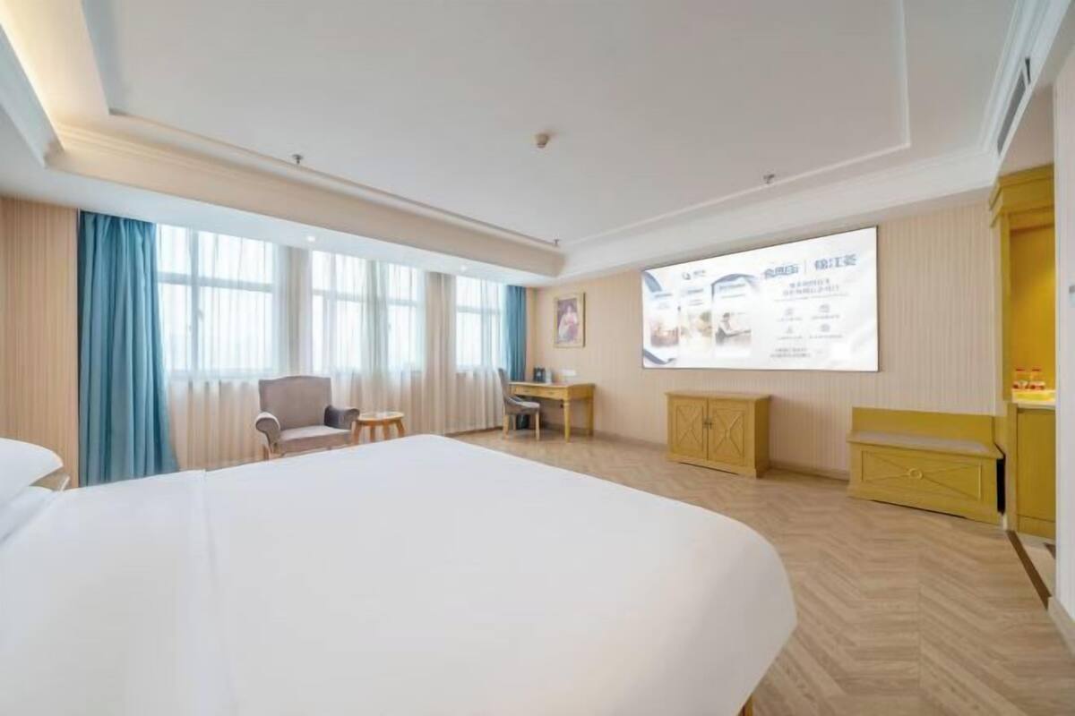 A hotel room with a large bed, a desk, a chair, and a wardrobe.